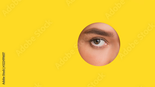 Female eye without mascara looking through round hole in paper