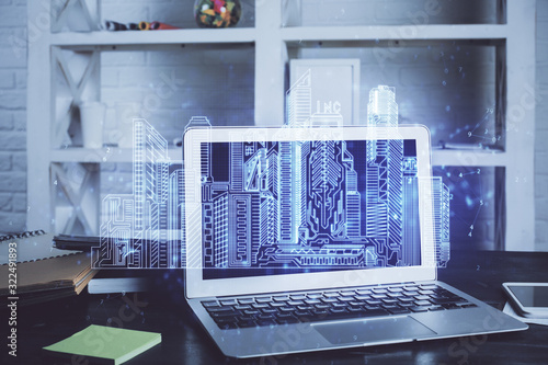 Desktop computer background in office and big town buildings hologram drawing. Double exposure. Smart city concept.