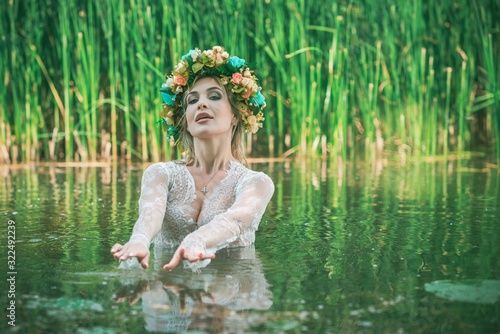 Fototapeta Naklejka Na Ścianę i Meble -  Romantic woman in flower hoop at hair, lace transparent dress in lake 
