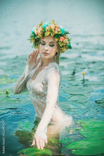 Romantic woman in flower hoop at hair, lace transparent dress in lake 