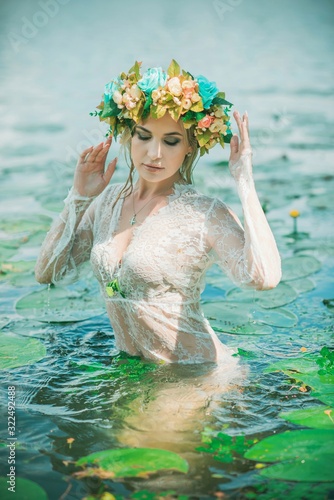 Romantic woman in flower hoop at hair, lace transparent dress in lake 