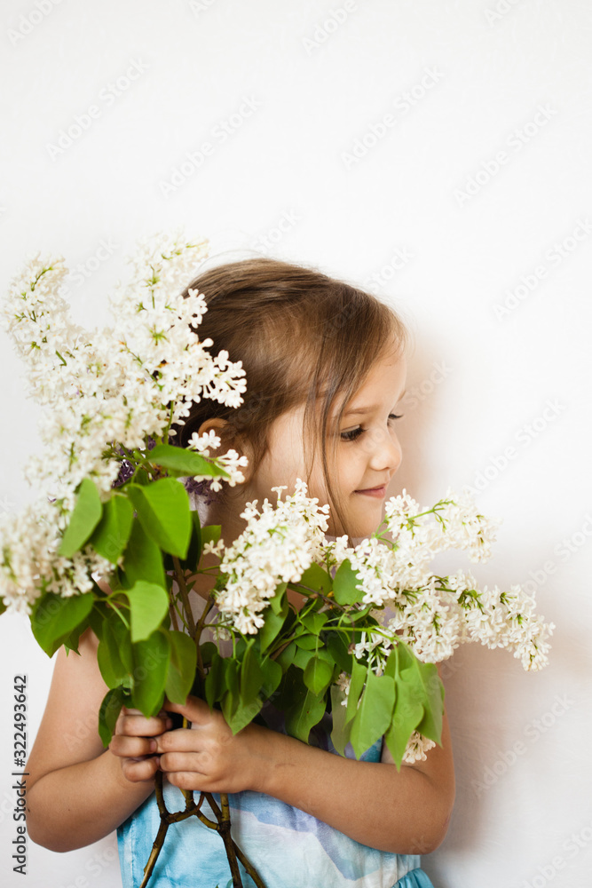 A little girl on a white background stands and holds branches of lilac, blooming kurst, lilac, spring and summer A little girl on a white background stands and holds branches of lilac, blooming kurst, lilac, spring and summer