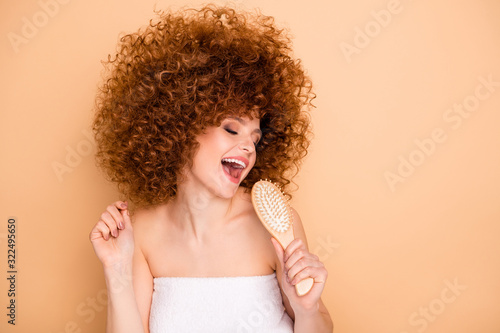 Close-up portrait of her she nice cute charming attractive lovely cheerful positive playful wavy-haired girl using comb like mic shower bath preparation isolated over beige pastel background