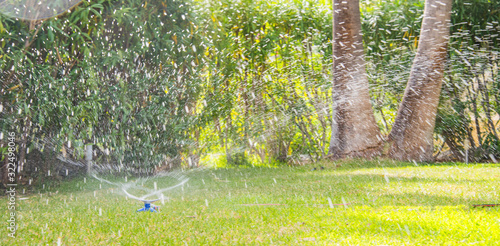 Lawn water sprinkler spraying water over lawn green fresh grass in garden