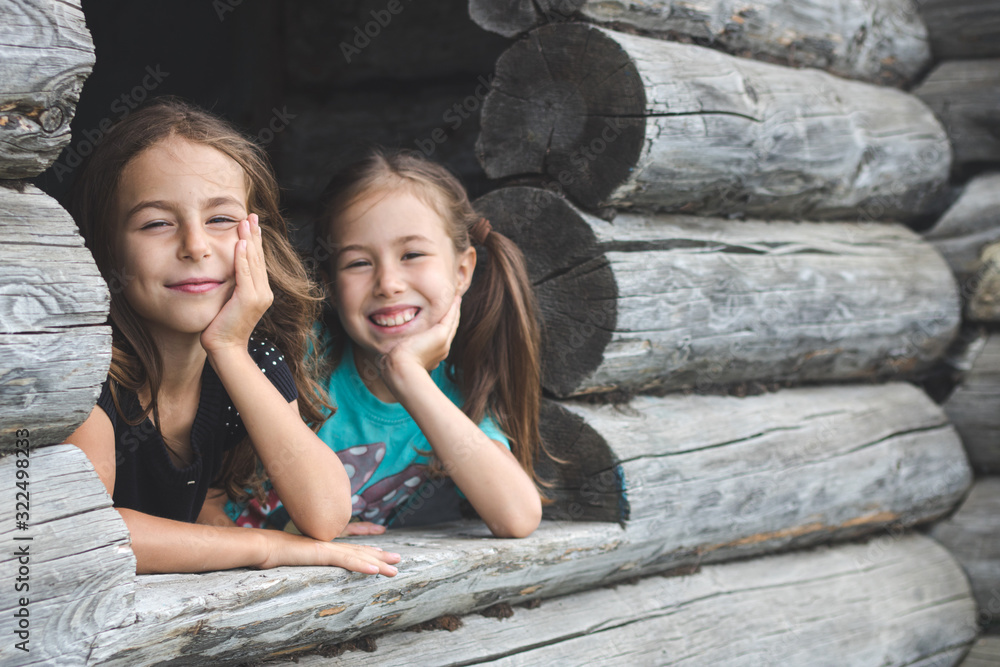 Children peep out the window of an old wooden house and smiling. Summer vacation in the country Children peep out the window of an old wooden house and smiling. Summer vacation in the country
