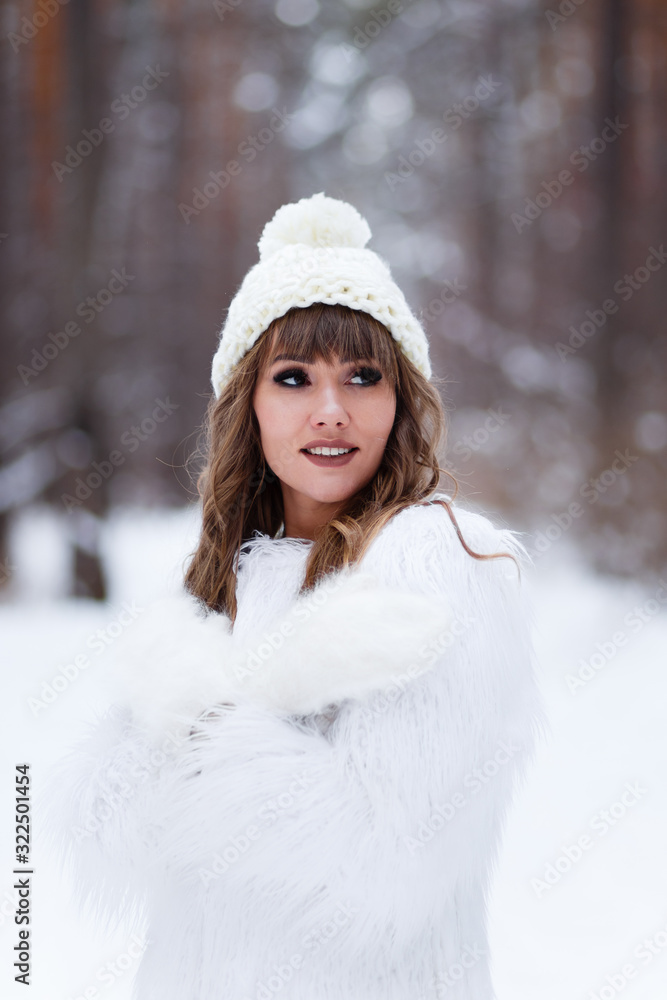A beautiful pretty young girl with curly hair and a snow-white smile in a white warm fur coat is walking and fooling around in the winter forest against the background of snow and trees, enjoying A beautiful pretty young girl with curly hair and a snow-white smile in a white warm fur coat is walking and fooling around in the winter forest against the background of snow and trees, enjoying