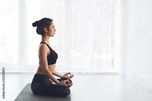 Fototapeta Naklejka Na Ścianę i Meble -  Side view of slim girl practicing yoga sitting on mat