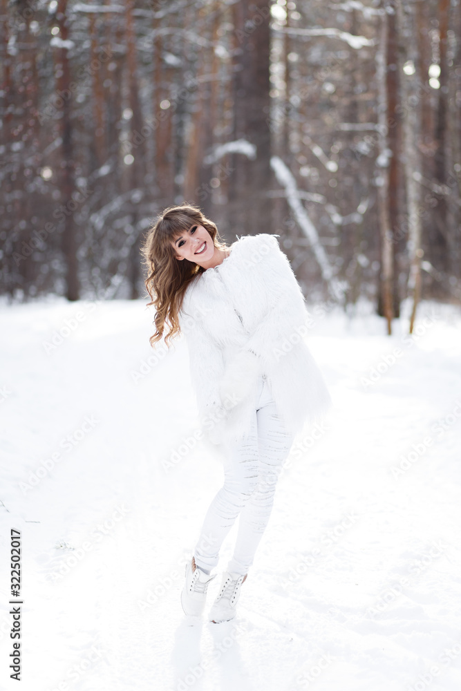 A beautiful pretty young girl with curly hair and a snow-white smile in a white warm fur coat is walking and fooling around in the winter forest against the background of snow and trees, enjoying A beautiful pretty young girl with curly hair and a snow-white smile in a white warm fur coat is walking and fooling around in the winter forest against the background of snow and trees, enjoying