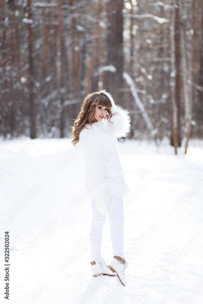 A beautiful pretty young girl with curly hair and a snow-white smile in a white warm fur coat is walking and fooling around in the winter forest against the background of snow and trees, enjoying A beautiful pretty young girl with curly hair and a snow-white smile in a white warm fur coat is walking and fooling around in the winter forest against the background of snow and trees, enjoying