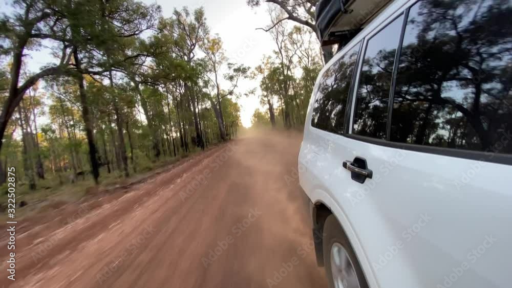 White SUV driving through forest on dusty gravel road looking backwards to the wheel White SUV driving through forest on dusty gravel road looking backwards to the wheel