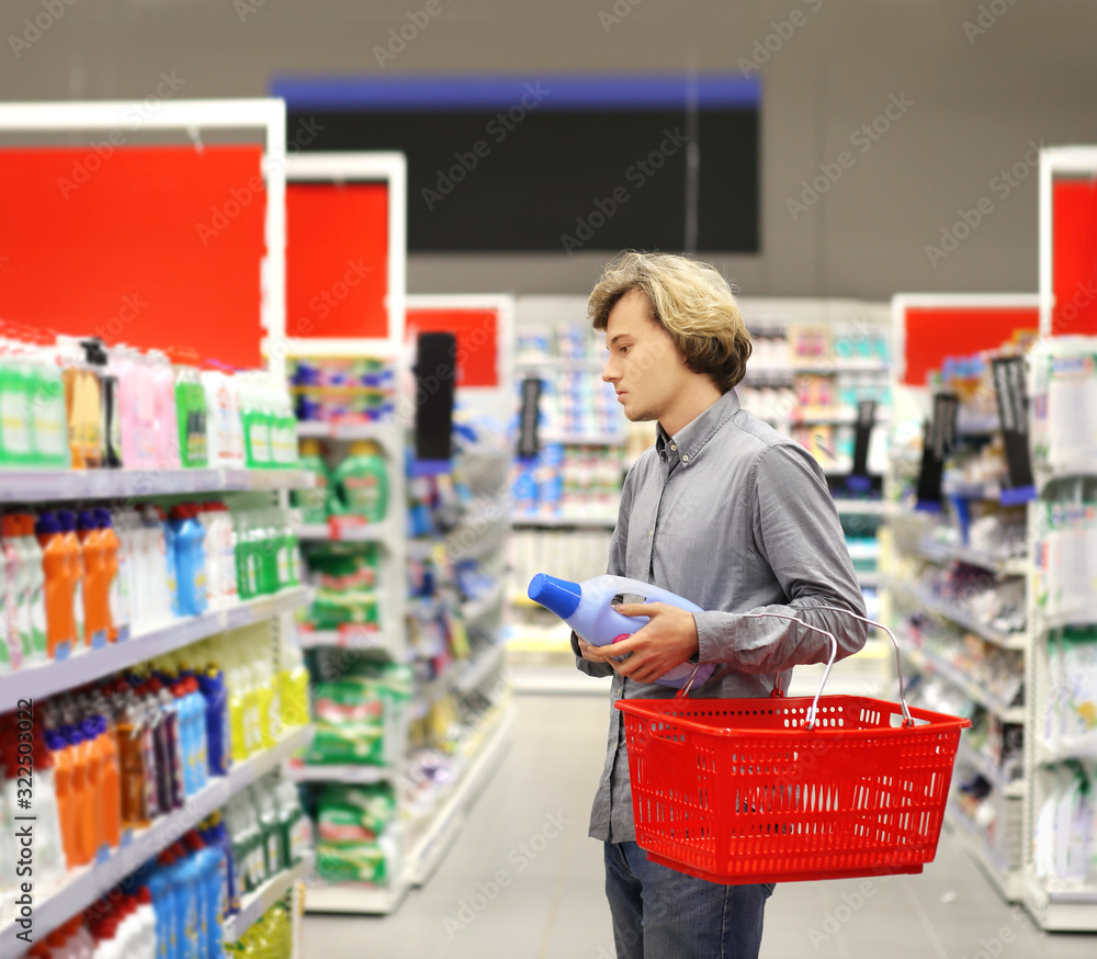 Man shopping in supermarket reading product information.(washing powder,detergent)	