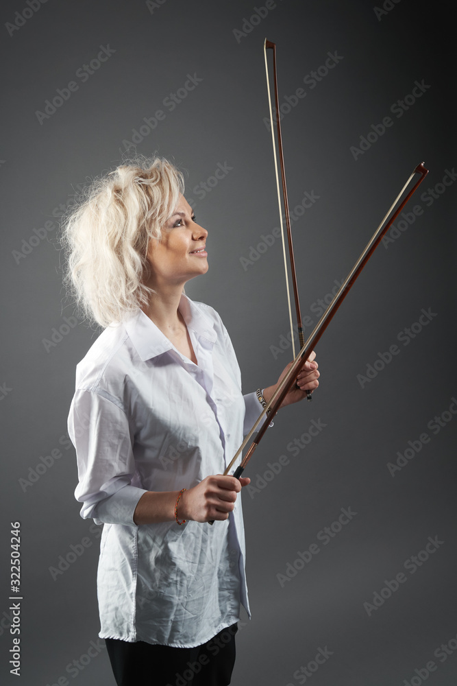 Studio shot of an young blonde caucasian girl violinist wearing a white shirt posing holding two violin bows Studio shot of an young blonde caucasian girl violinist wearing a white shirt posing holding two violin bows