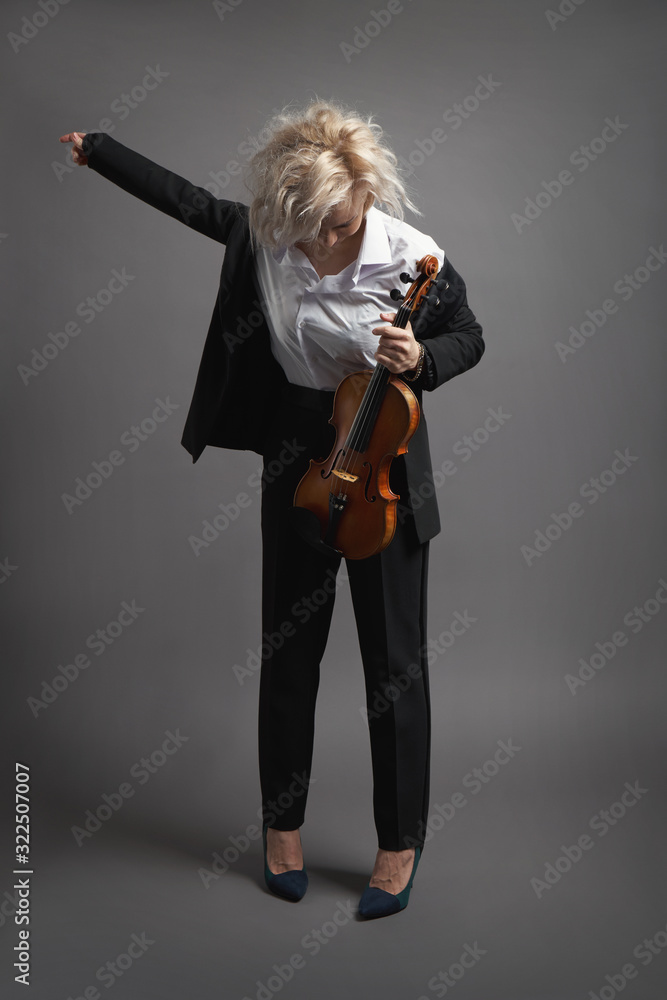 Fototapeta premium Young woman violinist in a black male suit with a violin putting on her jacket