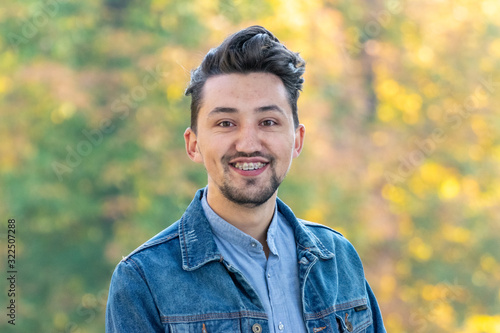 Handsome young man looking at the camera. Portrait of laughing confident and successful young man with a denim jacket and blue shirt outside. Happy guy smiling