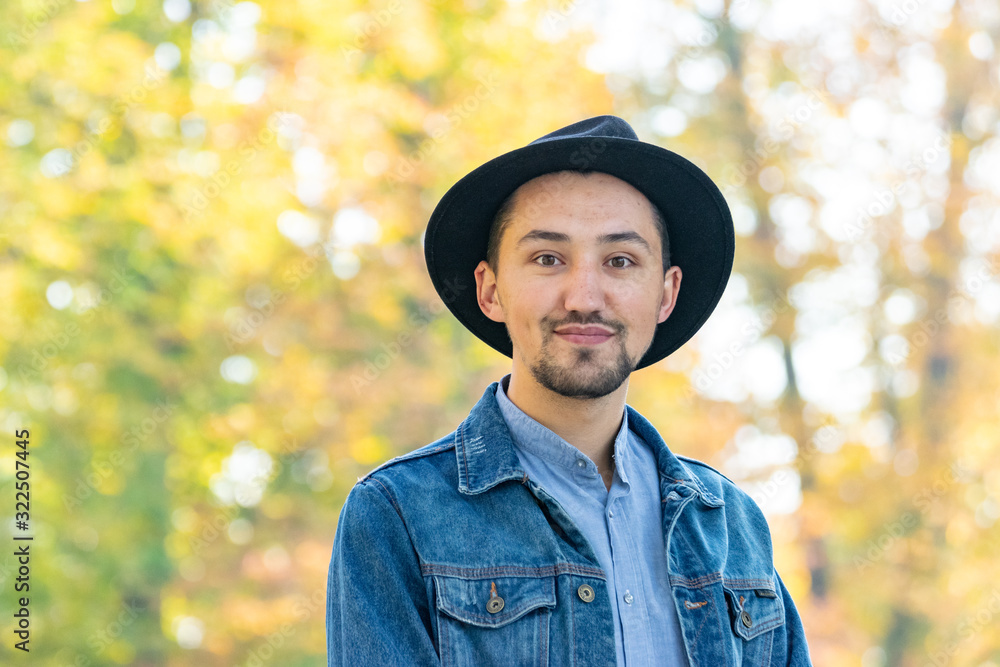 Handsome young man looking at the camera. Portrait of a confident and successful young man with a denim jacket and blue shirt outside. Happy guy smiling