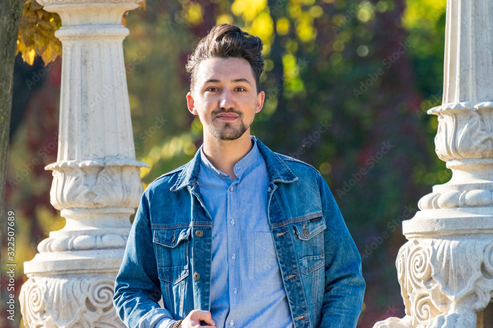 Handsome young man looking at the camera. Portrait of a confident and successful young man with a denim jacket and blue shirt outside. Happy guy smiling
