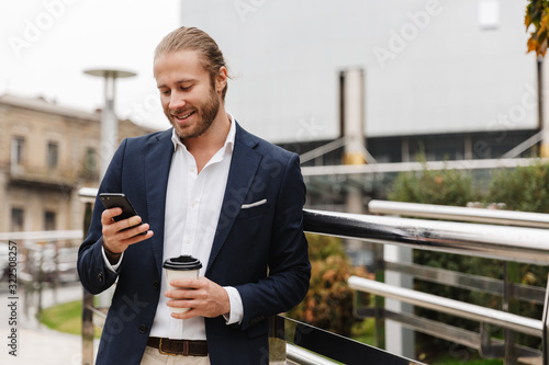Tableau sur toile Image of young businessman holding coffee cup and cellphone on city street