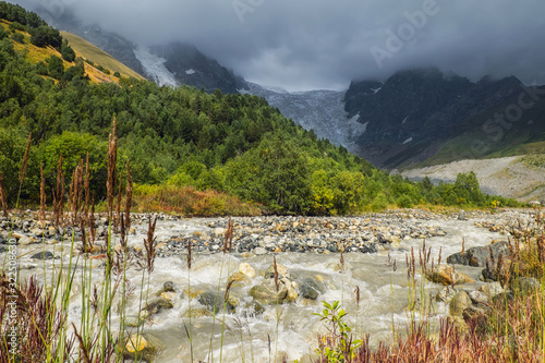 Strong mountain rocky river Adishchala and its source glacier Lardaad on a background in gloomy light photo