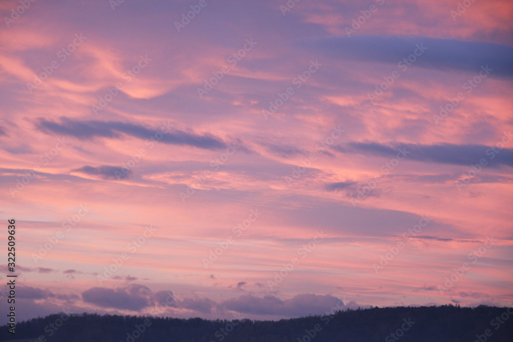 Dreamy evening sky in pastel tones with fluffy pink clouds at sunset over silhouette of hill country