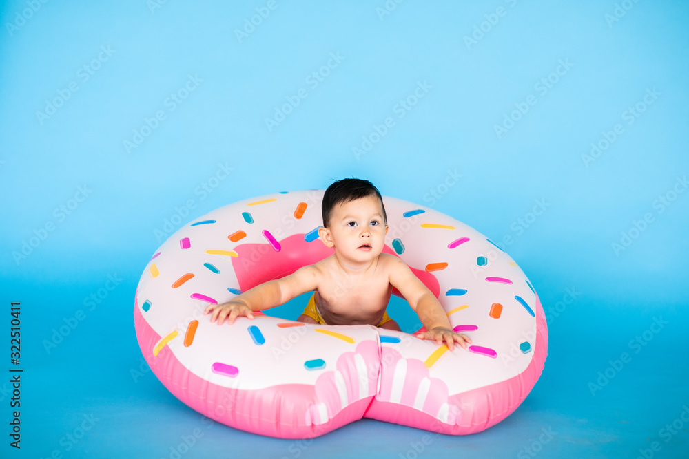 Happy baby boy in swimsuit with swimming ring donut on a colored blue background Happy baby boy in swimsuit with swimming ring donut on a colored blue background