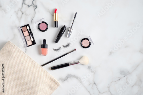 Makeup bag with cosmetic products spilling out on to marble table. Flat lay, top view. Stylish make up artist pouch with beauty products