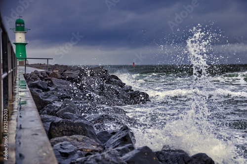 Lighthouse on the pier in Warnemuende during storm the waves break on the pier - Baltic Sea in Germany