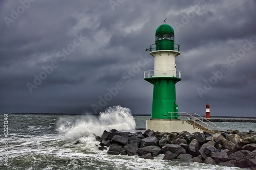 Lighthouse on the pier in Warnemuende during storm the waves break on the pier - Baltic Sea in Germany