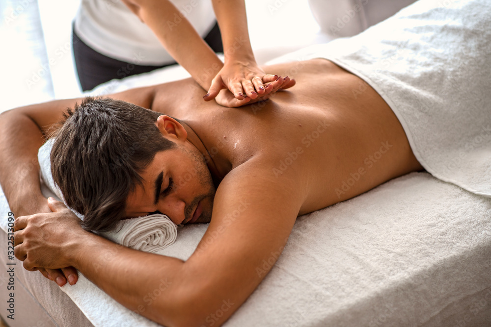 Sports massage. Massage therapist massaging shoulders of a male athlete,  working with Trapezius muscle. Toned image. Masseur doing massage on man  body in the spa salon. Beauty treatment concept. Stock Photo