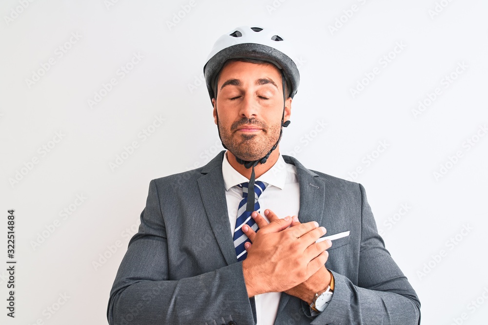 Young handsome business man wearing suit and tie and bike helmet over isolated background smiling with hands on chest with closed eyes and grateful gesture on face. Health concept. Young handsome business man wearing suit and tie and bike helmet over isolated background smiling with hands on chest with closed eyes and grateful gesture on face. Health concept.