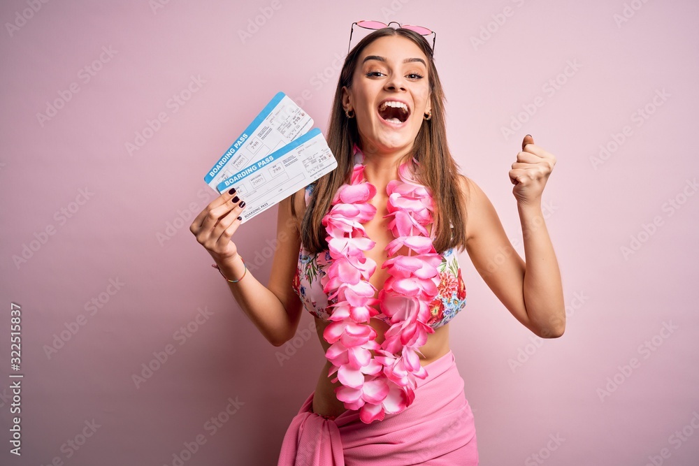 Young beautiful tourist woman on vacation wearing bikini and hawaiian lei holding boarding pass screaming proud and celebrating victory and success very excited, cheering emotion Young beautiful tourist woman on vacation wearing bikini and hawaiian lei holding boarding pass screaming proud and celebrating victory and success very excited, cheering emotion