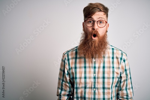 Handsome Irish redhead man with beard wearing glasses and hipster shirt afraid and shocked with surprise expression, fear and excited face.