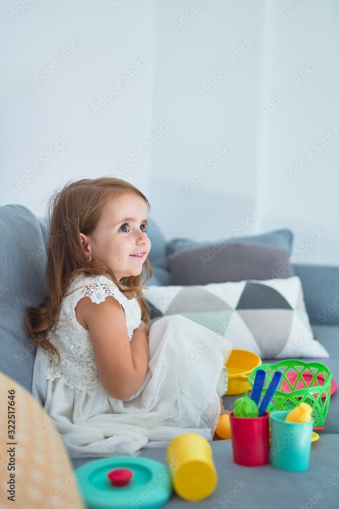 Adorable blonde toddler siting on the sofa cooking with food and cutlery toys at home Adorable blonde toddler siting on the sofa cooking with food and cutlery toys at home