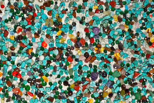 Texture of various jewels on a white background. Blue, yellow and red stones. Beads and necklaces are glued to the wall.
