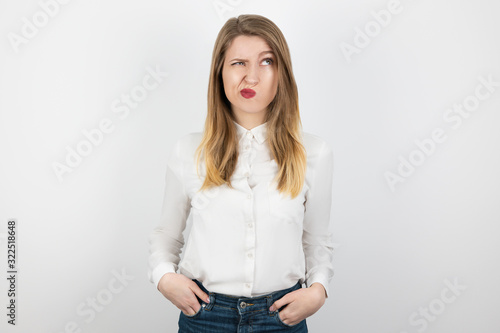 young beatuiful blond woman looks hesitant standing on isolated white background, body language