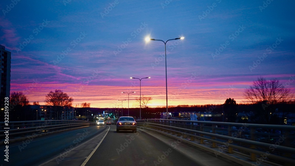 Beautiful colorful sunset in the city. Cars driving on the road during dawn.
