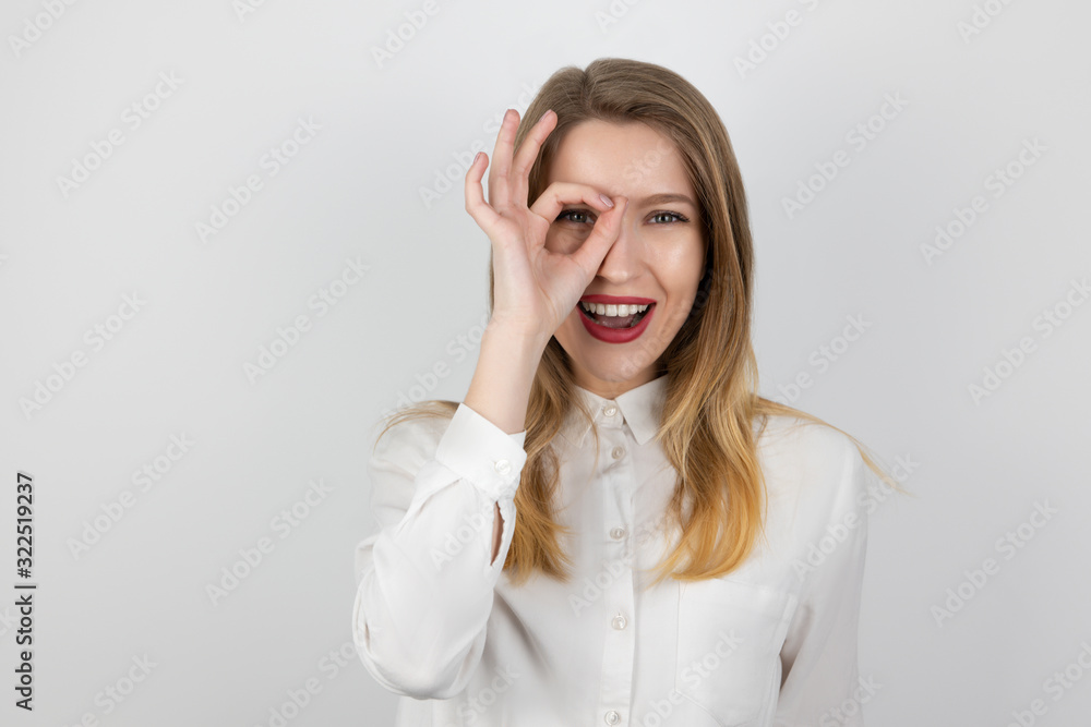 young beatuiful blond woman holding her hand like magnifying glass near her eye looks surprised, splash of emotions