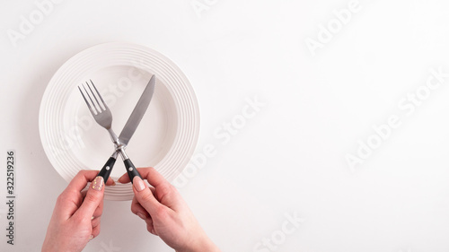 Top view of female hands with fork, knife and empty plate on white background. Woman on diet. Space for text