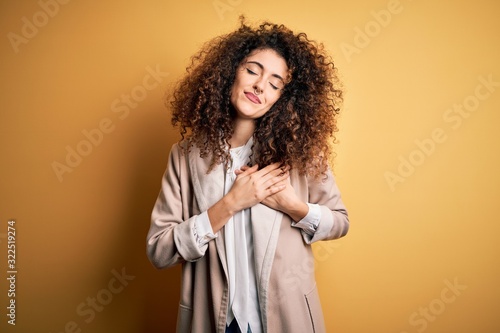 Young beautiful brunette woman with curly hair and piercing wearing casual t-shirt and diadem smiling with hands on chest with closed eyes and grateful gesture on face. Health concept.