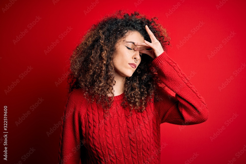 Young beautiful woman with curly hair and piercing wearing casual red sweater tired rubbing nose and eyes feeling fatigue and headache. Stress and frustration concept.