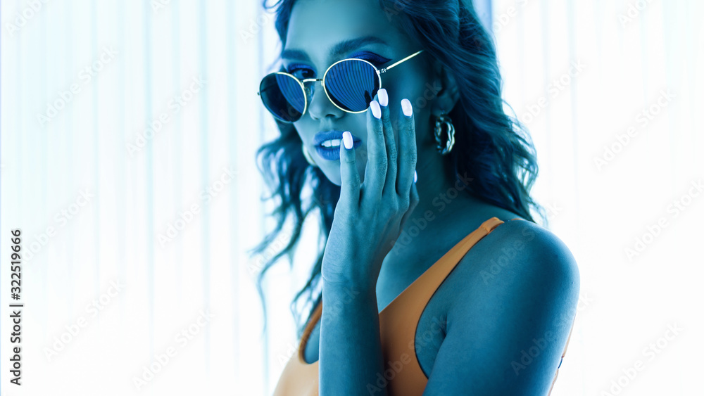 Pretty beautiful sensual young hipster woman in sunglasses in a stylish swimsuit with trendy manicure enjoys ultraviolet rays in a solarium. Portrait of a sexy girl with tanned skin in a tanning bed. - obrazy, fototapety, plakaty 