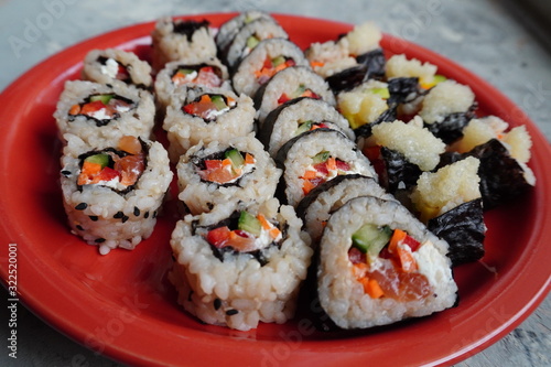 Set of homemade sushi or rolls with salmon, sesame seeds serving on red plate on grey background, cooking at home.