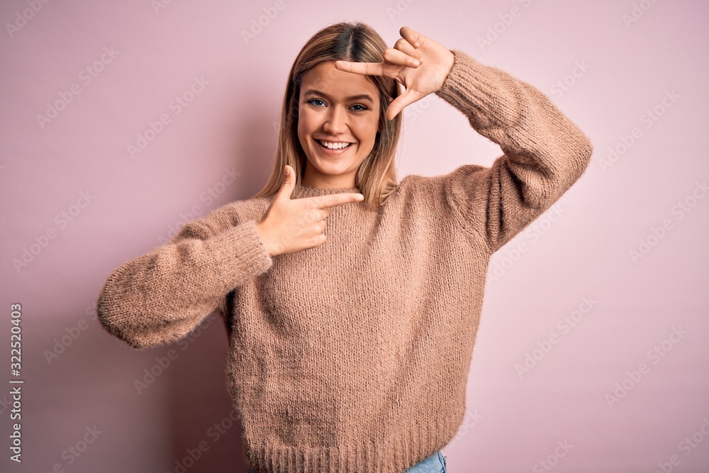 Young beautiful blonde woman wearing winter wool sweater over pink isolated background smiling making frame with hands and fingers with happy face. Creativity and photography concept. Young beautiful blonde woman wearing winter wool sweater over pink isolated background smiling making frame with hands and fingers with happy face. Creativity and photography concept.