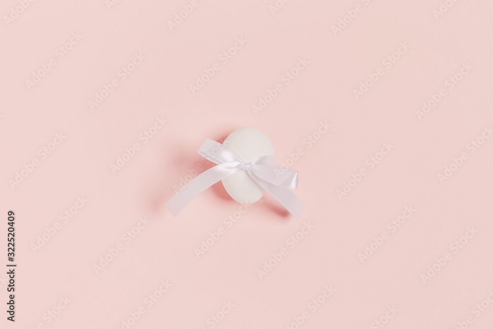 Happy Easter. One white egg inside ribbon bow on pink background. Flat lay, top view, copy space. Happy Easter. One white egg inside ribbon bow on pink background. Flat lay, top view, copy space.