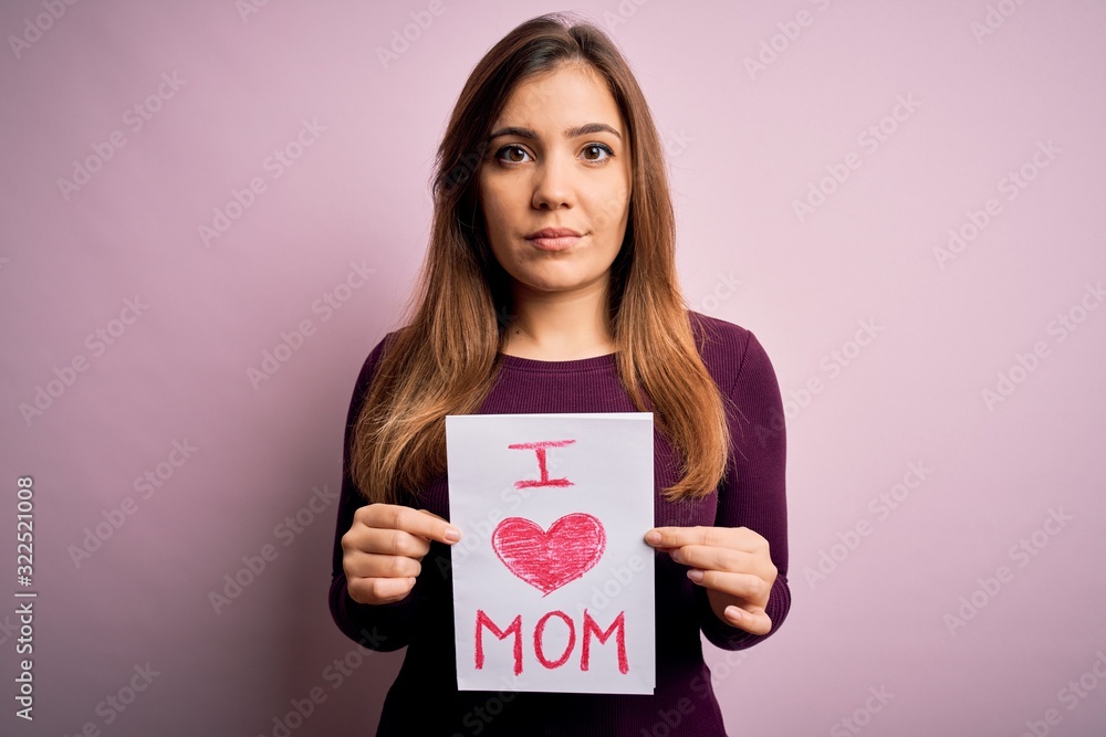 Young beautiful woman holding paper with love mom message celebrating mothers day with a confident expression on smart face thinking serious Young beautiful woman holding paper with love mom message celebrating mothers day with a confident expression on smart face thinking serious