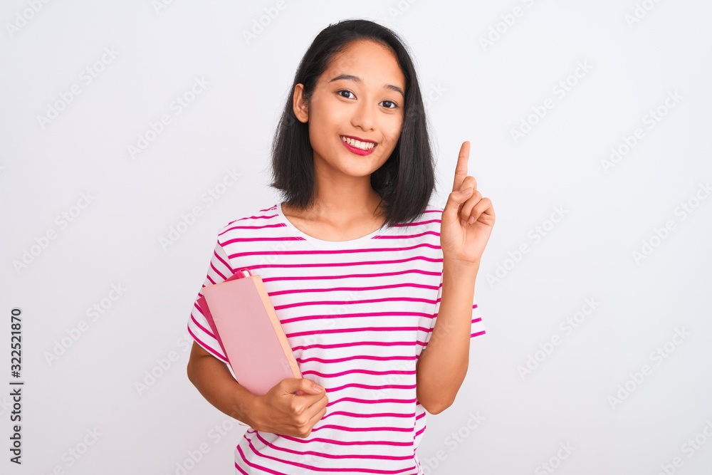 Young beautiful chinese woman holding books standing over isolated white background surprised with an idea or question pointing finger with happy face, number one Young beautiful chinese woman holding books standing over isolated white background surprised with an idea or question pointing finger with happy face, number one