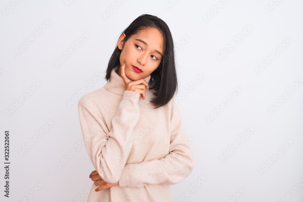Young chinese woman wearing turtleneck sweater standing over isolated white background with hand on chin thinking about question, pensive expression. Smiling with thoughtful face. Doubt concept. Young chinese woman wearing turtleneck sweater standing over isolated white background with hand on chin thinking about question, pensive expression. Smiling with thoughtful face. Doubt concept.