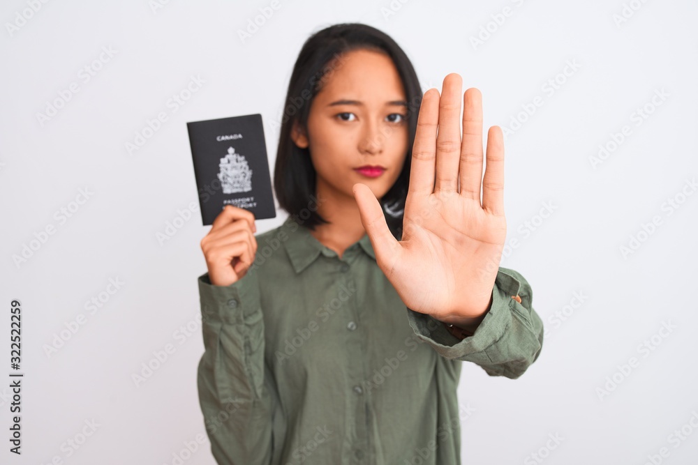 Beautiful chinese woman holding Canada Canadian passport over isolated white background with open hand doing stop sign with serious and confident expression, defense gesture Beautiful chinese woman holding Canada Canadian passport over isolated white background with open hand doing stop sign with serious and confident expression, defense gesture