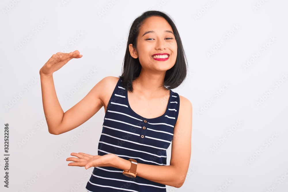 Young chinese woman wearing striped t-shirt standing over isolated white background gesturing with hands showing big and large size sign, measure symbol. Smiling looking at the camera. Measuring Young chinese woman wearing striped t-shirt standing over isolated white background gesturing with hands showing big and large size sign, measure symbol. Smiling looking at the camera. Measuring