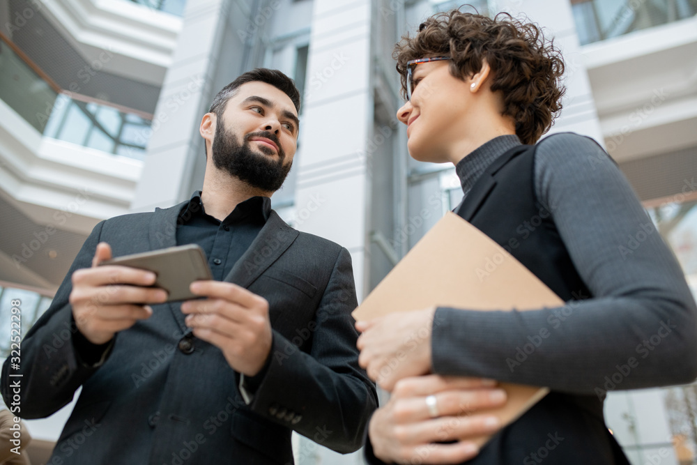 Below view of young ambitious business partners in formalwear discussing web project using smartphone in office Below view of young ambitious business partners in formalwear discussing web project using smartphone in office