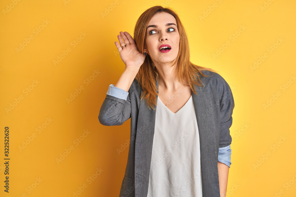 Redhead caucasian business woman over yellow isolated background smiling with hand over ear listening an hearing to rumor or gossip. Deafness concept. Redhead caucasian business woman over yellow isolated background smiling with hand over ear listening an hearing to rumor or gossip. Deafness concept.